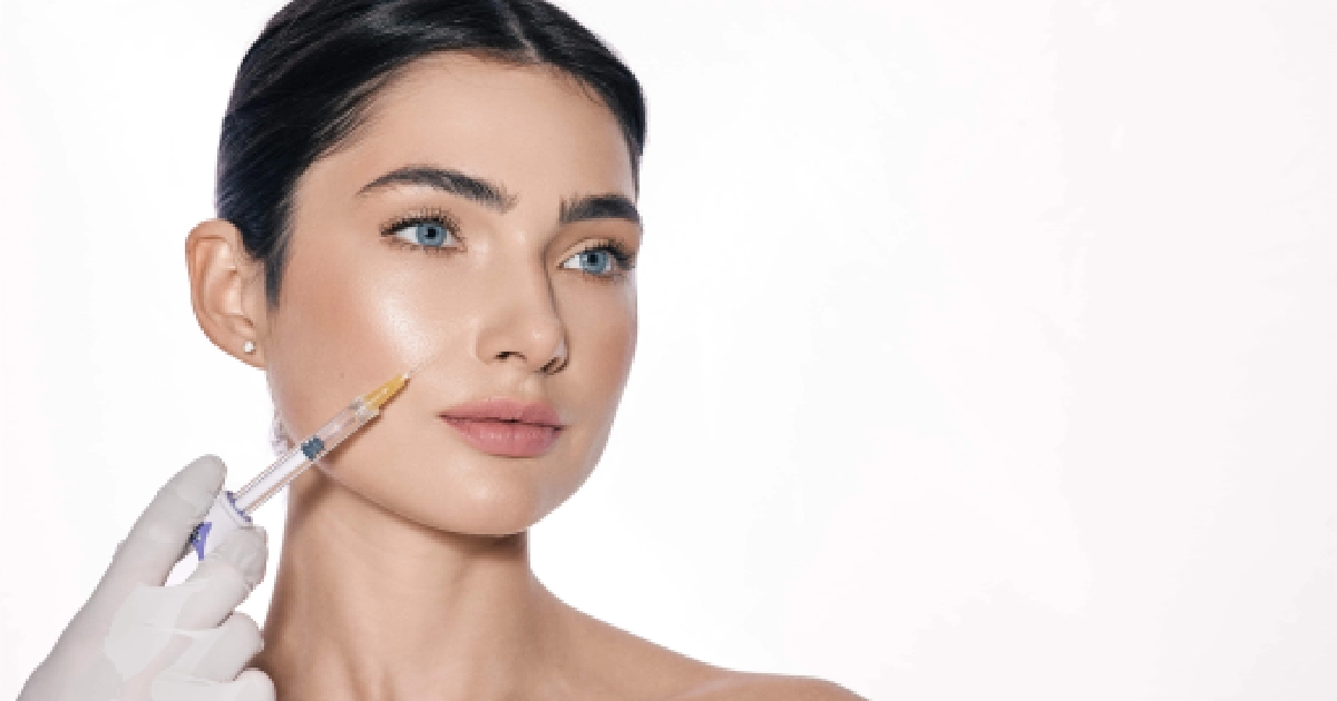 Close-up of a woman with glowing skin receiving a dermal filler injection in Brookfield, WI, from a gloved hand, looking off-camera against a white background.